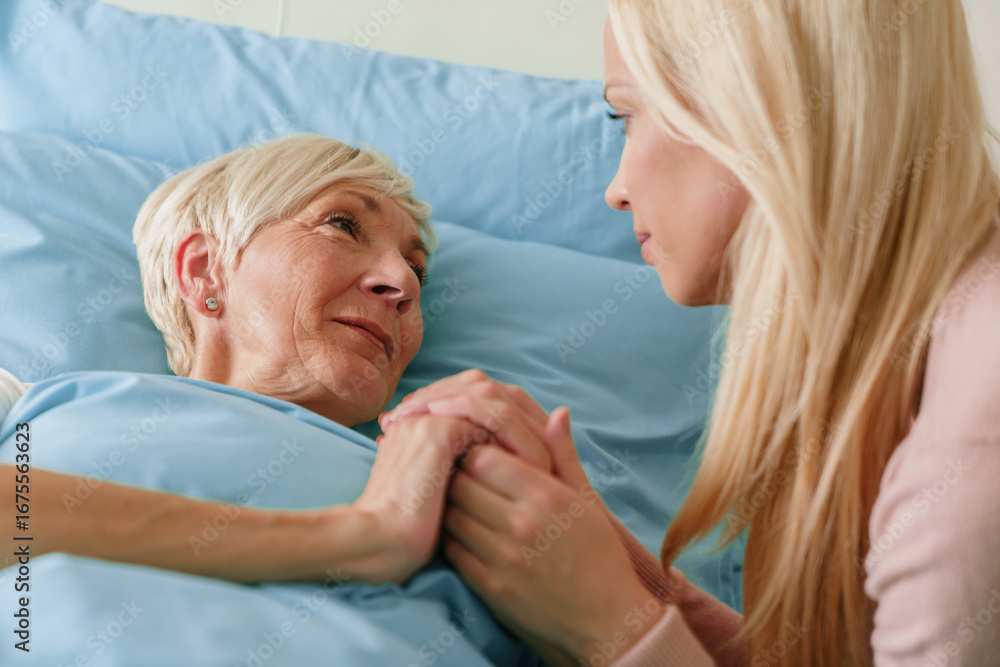 Obraz premium Blonde Woman Comforting Elderly Grandmother in a Hospital Room with Warm Lighting and Emotional Connection