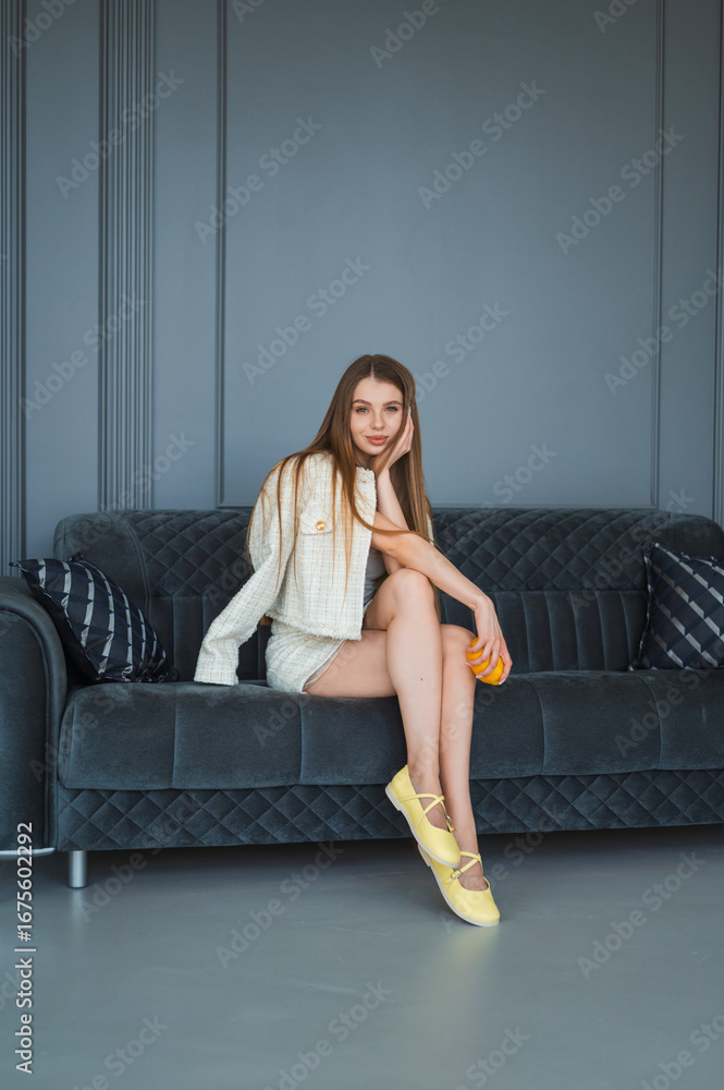 Obraz premium Joyful Moments with Citrus A Stylish Woman Relaxing on a Sofa showcasing her fashion sense and cheerful demeanor.
