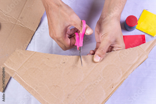 hands cutting cardboard with scissors for DIY craft project, creativity, recycling, and handmade work concept.