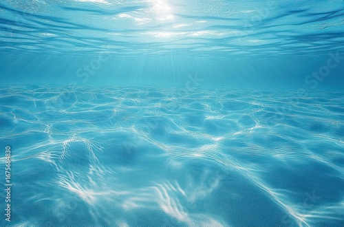 Clear blue underwater scene with sunlight rays penetrating gently through water surface onto rippled sandy seabed