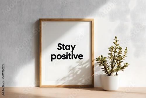 Frame with stay positive quote and plant on wooden table.
