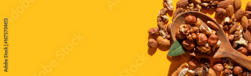 Different nuts, walnut, hazelnut, almond in wooden spoon on yellow background flat lay top view. Mix of tasty healthy nuts, snack, appetizer. Sunlight with long shadows. Long banner. Space for text