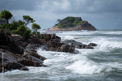 Rocky coast with waves crashing against rocks small island with building in the background overcast sky
