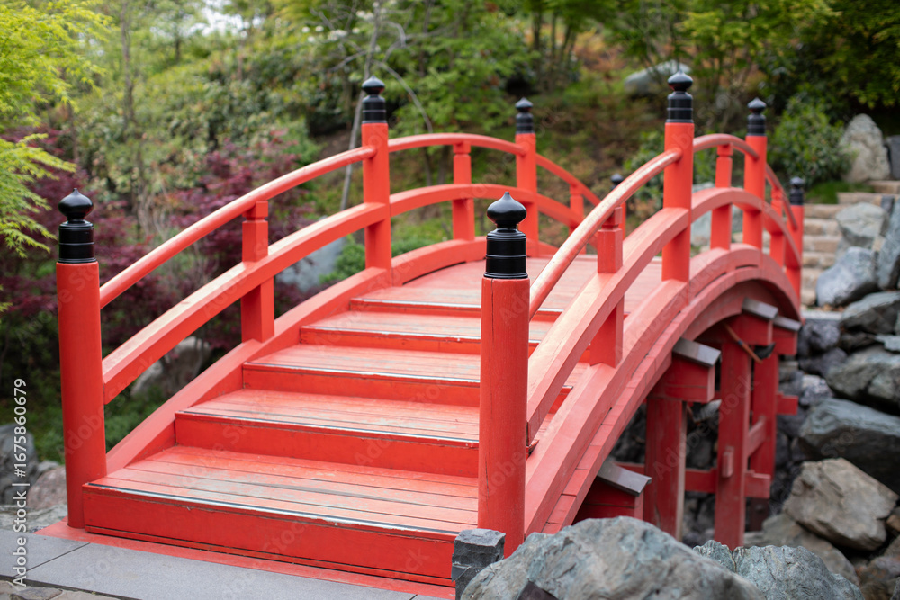 Red bridge with a curved design, featuring black posts and a wooden deck. The bridge is surrounded by greenery and rocks, creating a natural and serene environment.
Red bridge with a curved design, featuring black posts and a wooden deck. The bridge is surrounded by greenery and rocks, creating a natural and serene environment.