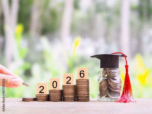 Hand putting coin into stack of coins, Glass bottle with graduation hat. The concept of saving money for education, student loan, scholarship, tuition fees in year 2026