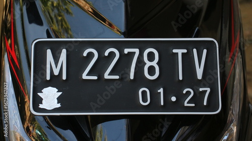 Closeup of an Indonesian motorcycle license plate mounted on a black vehicle, showing registration code and expiration date in bold white characters.