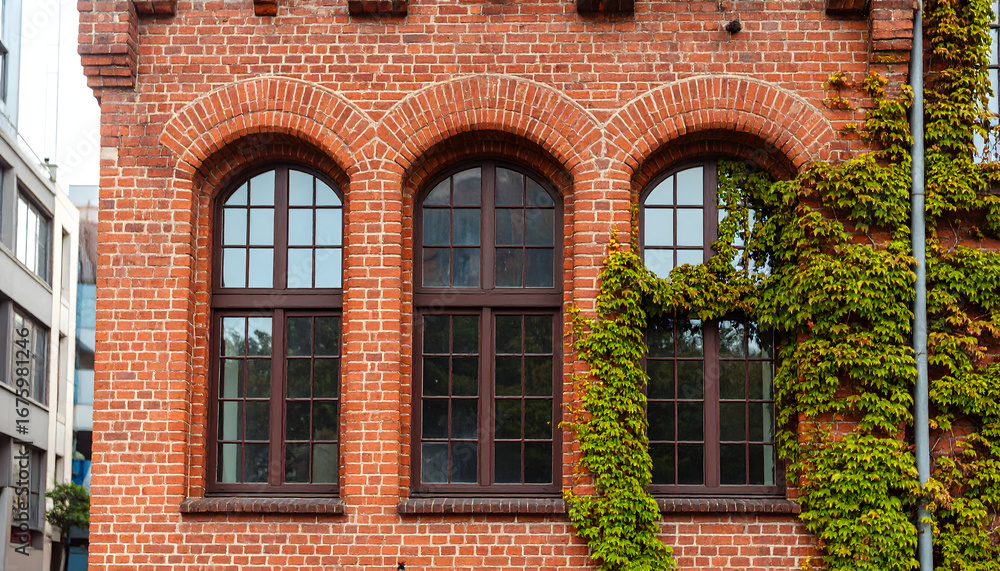 Fototapeta premium Facade of a Classic Red Brick Building with Arched Windows and Green Ivy