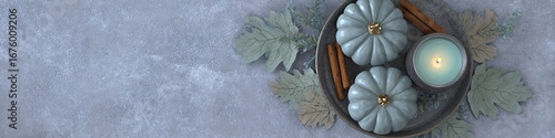 Blue pastel pumpkins with cinnamon sticks, candle and delicate leaves on light blue-gray background, flat lay