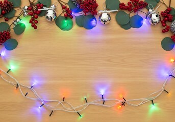Festive holiday border with eucalyptus, berries, silver bells, and colorful lights on wood