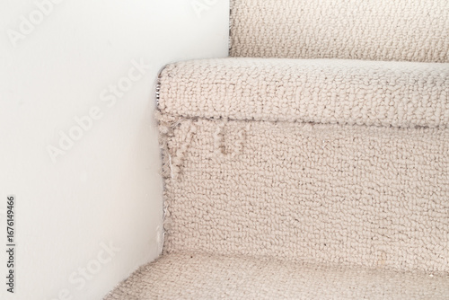 Frayed carpet on stairstep with fibers hanging of the edge. Close up of old home interior carpeted staircase with damage. Cat scratching, damaging or destroying staircase. Selective focus.
