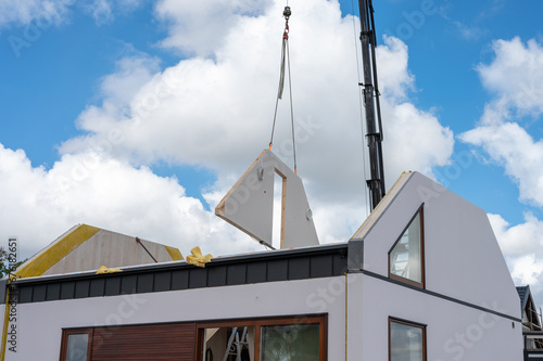 Crane lifting prefabricated wall panel onto modern modular house under construction.