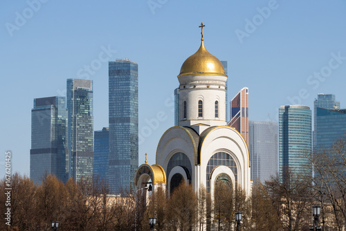A beautiful church against the backdrop of high-rise buildings. Modern city landscape. View of the church and skyscrapers. Tradition and modernity. Church of St. George the Victorious, Moscow, Russia.