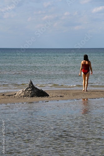 Women in red bathing suit standing on a sandbar in Denmark and looking out to sea.