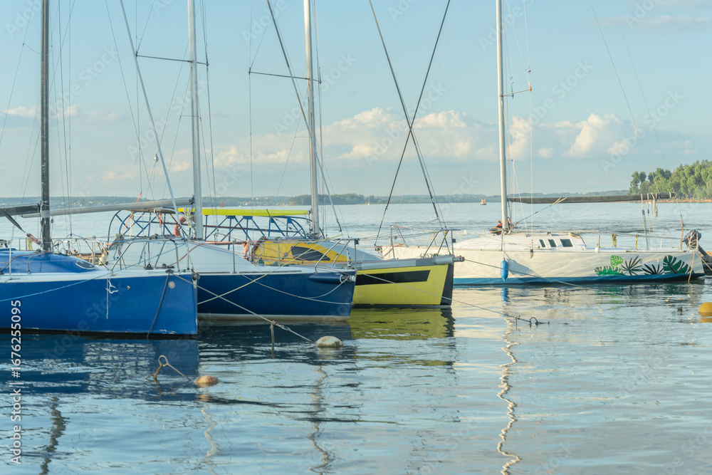 Fototapeta premium Sailboats docked at quiet marina under clear blue sky. Yachts moored quietly in the harbor, poised for new journeys beneath an endless sky of freedom and possibility.