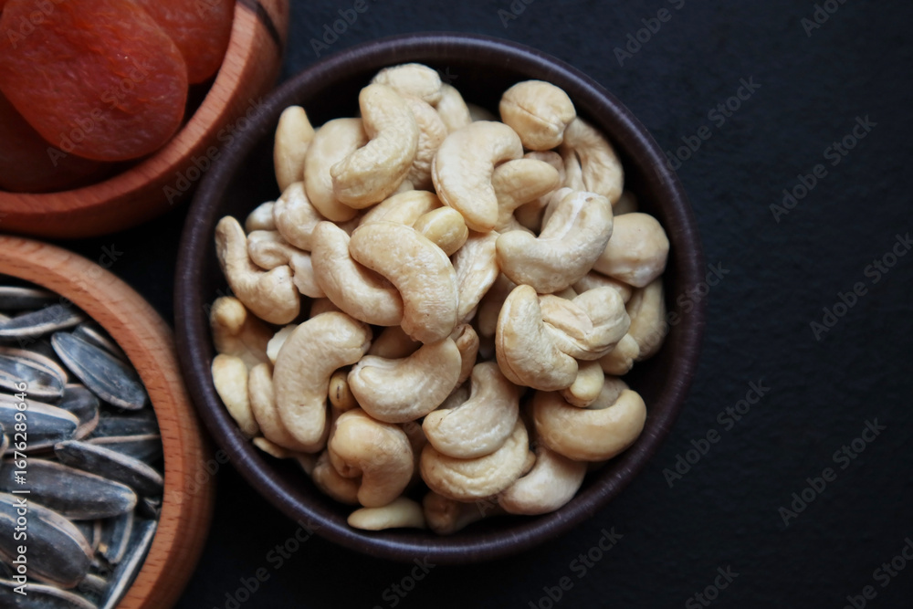 Fototapeta premium Unroasted, raw cashews were designed in a bamboo bowl on black surface