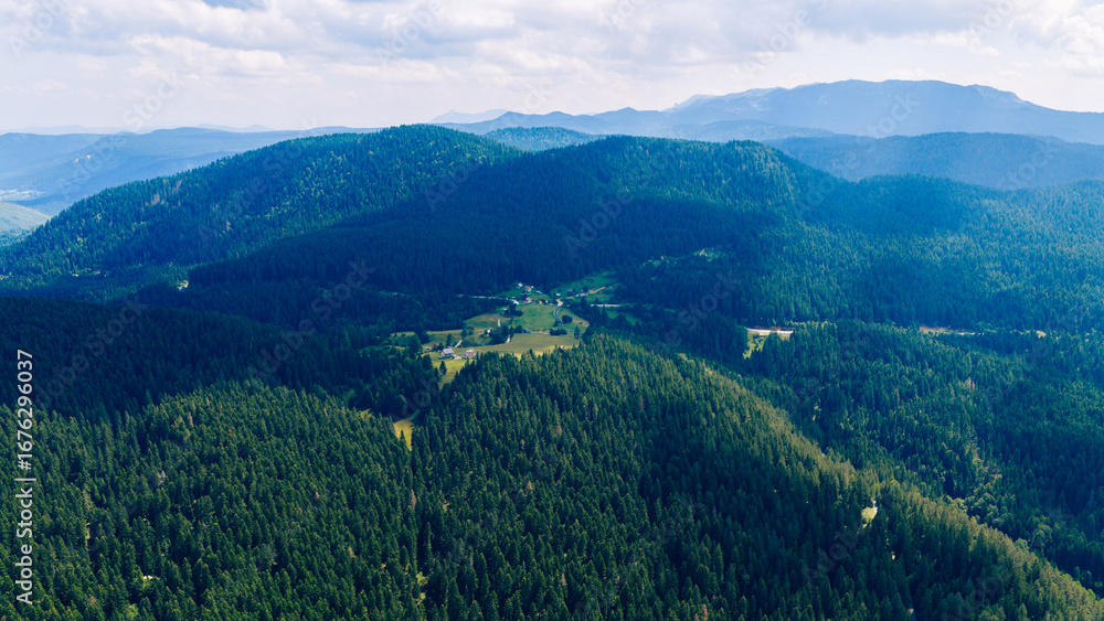 Fototapeta premium Aerial view of Trebević mountain with its green slopes, forested ridges, and panoramic view of Sarajevo region under summer sky