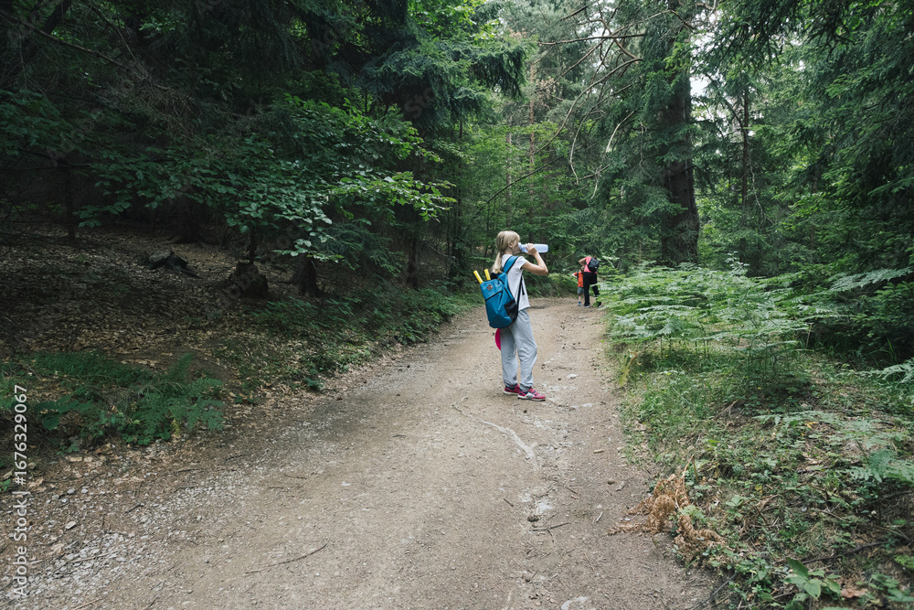 Obraz premium Short break while hiking. A girl drinks water.