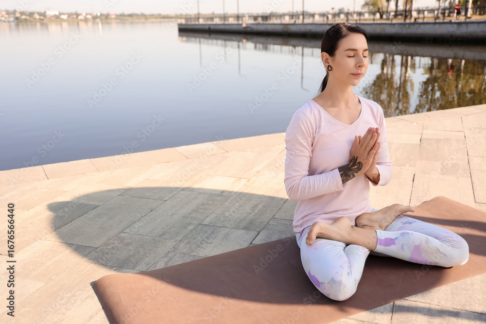 Fototapeta premium Young woman meditating on embankment