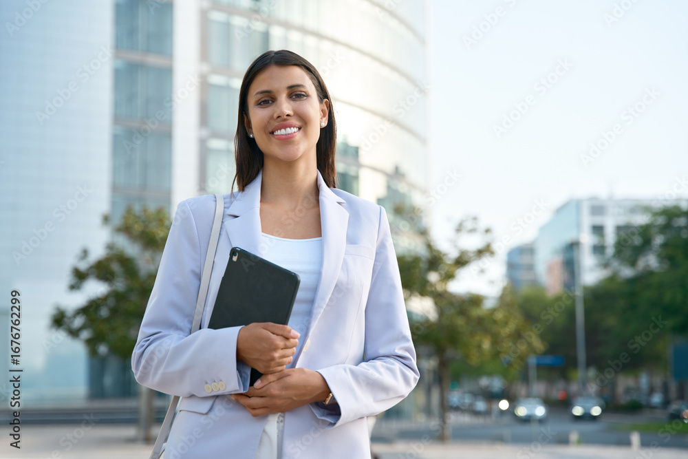Fototapeta premium Portrait of businesswoman investor holding digital tablet using fintech tab app standing outdoors at business office. Mature latin Hispanic adult professional business woman looking smiling at camera