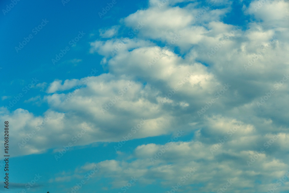 Obraz premium Fluffy white clouds scattered across a vibrant blue sky during a sunny afternoon in early autumn