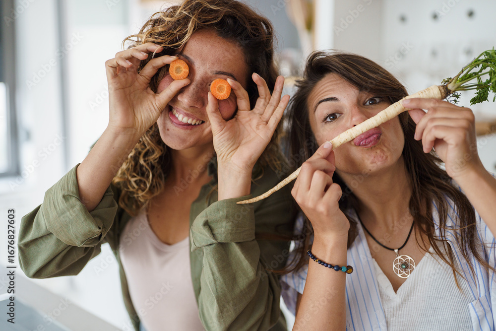 Fototapet Young Women Cooking Together in a Bright Kitchen Playing with Fresh Vegetables i