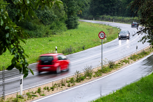 Cars driving along a country highway with a sign indicating a 70 kilometer per hour speed limit