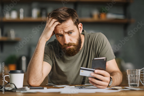 Man holding phone and credit card sitting at table with bills