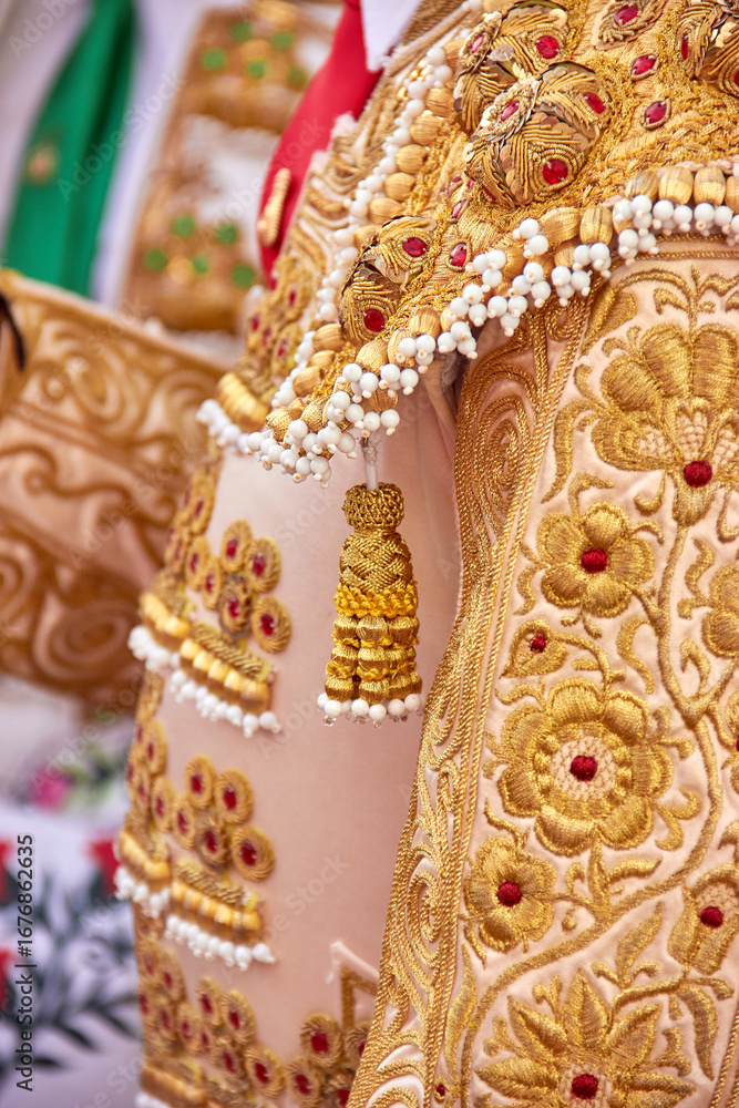 Naklejka premium Close-up of ornate gold embroidery on a matador’s traje de luces during a Practical lesson at Corrida School, Novillada. craftsmanship, culture