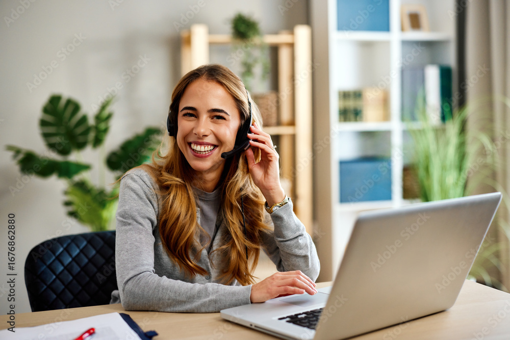 Obraz premium Happy female entrepreneur working remotely using laptop and headset in home office