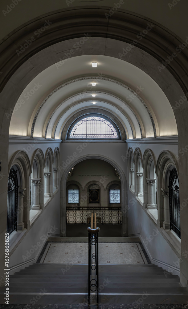Fototapeta premium a grand staircase with a prominent wooden handrail leading towards a large arched window at the top, and is flanked by arched hallways on either side within the National Portrait Gallery in London.
