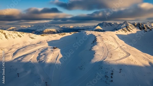 Winter mountain aerial view shows ski slopes, peaks, chairlifts, and wispy, colorful clouds