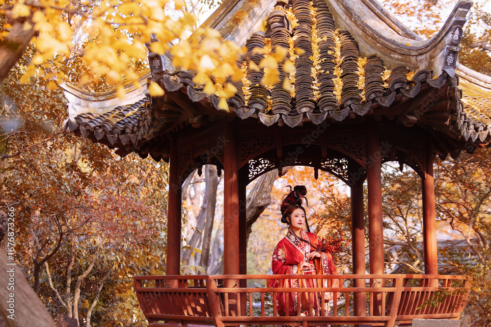 Fototapeta premium Woman in traditional red hanfu poses gracefully in an autumn garden pavilion Chinese word means autumn.