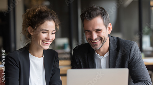 Two smiling professionals a man and a woman looking at a laptop