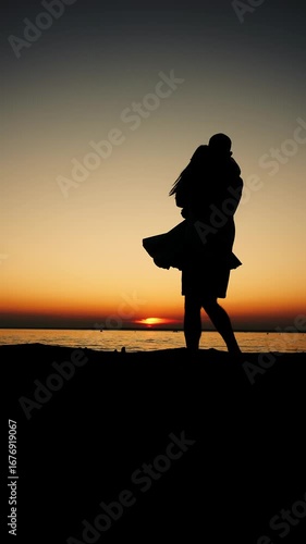 Silhouette of a young couple in love on the seashore at sunset, a man twirling a woman. Lovers enjoying a joint holiday at the sea. Vertical video.