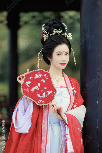 Graceful woman in traditional attire holding a decorative fan outdoors Chinese word means fan.