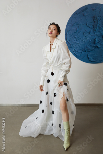 Fashionable woman in a white polka dot dress striking a pose indoors.