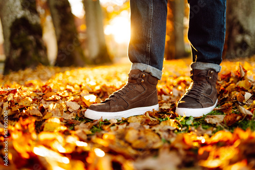 Canvas Print A close-up of a man in boots walking along a path strewn with bright autumn leaves