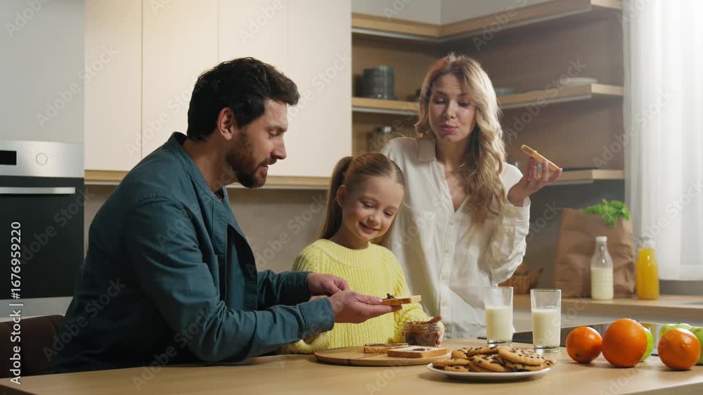 Happy Caucasian family at kitchen dad father man help custody adopted child girl daughter smear peanut chocolate paste on slice of bread mother mom eat delicious sandwich cooking breakfast together