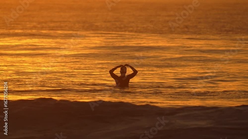 Male surfer sits on his surfboard in Indian Ocean and show a heart sign at sunset time. Powerful wave crashing behind his body.Maldives