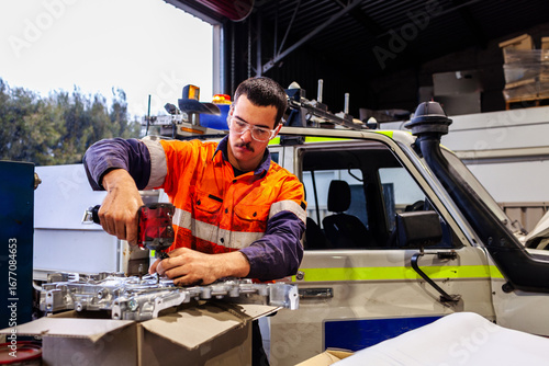 Aussie mechanic working on car engine repairs in workshop wearing high vis