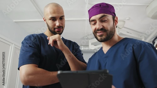 Two diverse doctors, one African-American and one Middle Eastern, collaborate in a bright hospital room, focused on a tablet. Surgeons in Operating Room