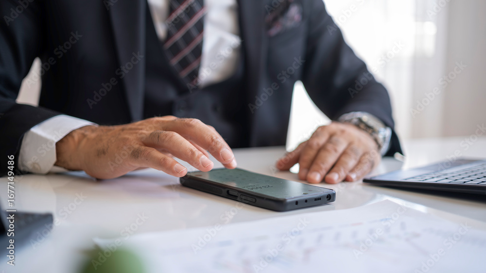 Obraz premium Businessman doing calculations with smart mobile phone at office desk.