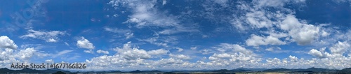 Panoramic view of a vibrant blue sky dotted with fluffy white clouds  with a faint line of distant mountains at the horizon