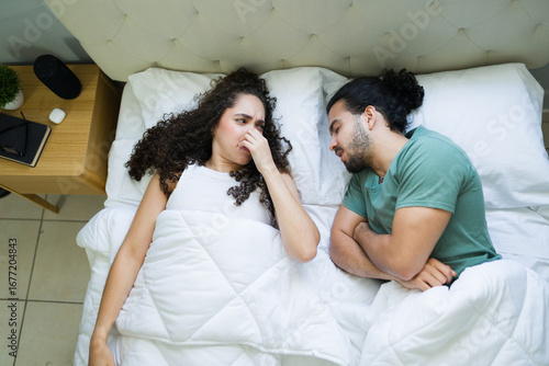 Woman pinching her nose because of bad breath from her partner sleeping in bed