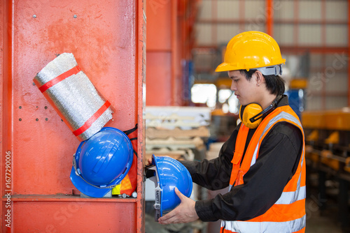 Fotografie Industrial worker in safety vest and helmet placing blue hard hat on storage shelf inside factory