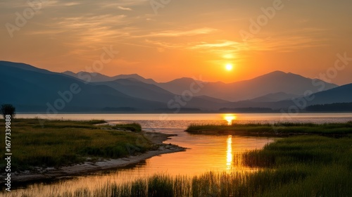 Wallpaper Mural A tranquil sunset over a lake with mountains in the background and grassy shoreline reflecting golden sunlight Torontodigital.ca