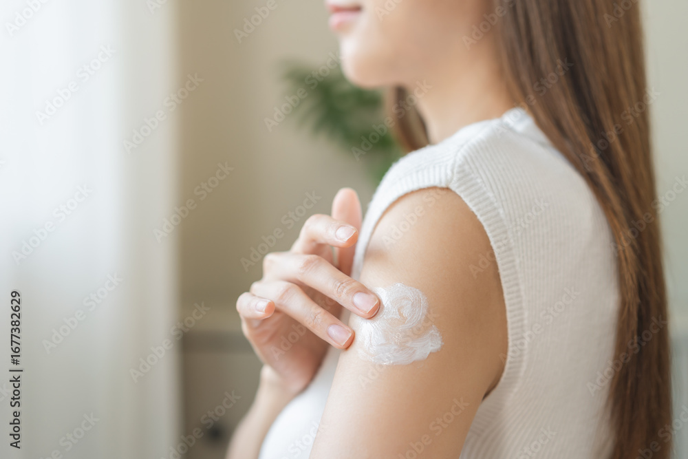 Naklejka premium Health skin care, beauty smile asian young woman, girl hand applying, putting moisturizer on her arm, shoulder after shower bath at home. Skin body cream moisturizing lotion, routine in the morning.