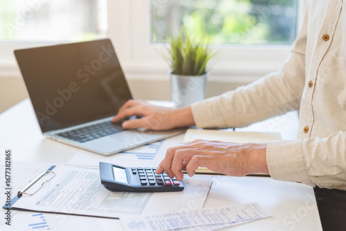 Account finance, asian young business man hand using calculator, laptop computer for calculate budget, cost and income of company from paperwork, plan spend money expenses, working on desk at home.