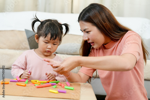 Asian single mother teaching little daughter assembling colorful clay pieces into creative shapes on table sitting together cozy bright living room early childhood education home learning