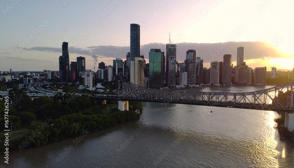 Naklejka premium A panoramic cityscape view of Brisbane, Australia's downtown area at sunset, featuring the iconic Story Bridge spanning a calm river.